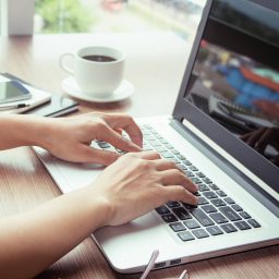 Hands on the keyboard of a laptop with coffee in the background
