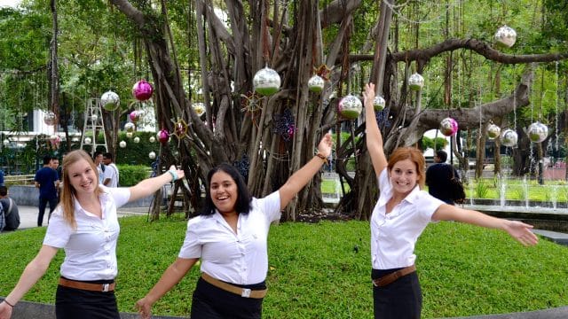 Three young women with a tree decorated in globes and other ornaments in the background