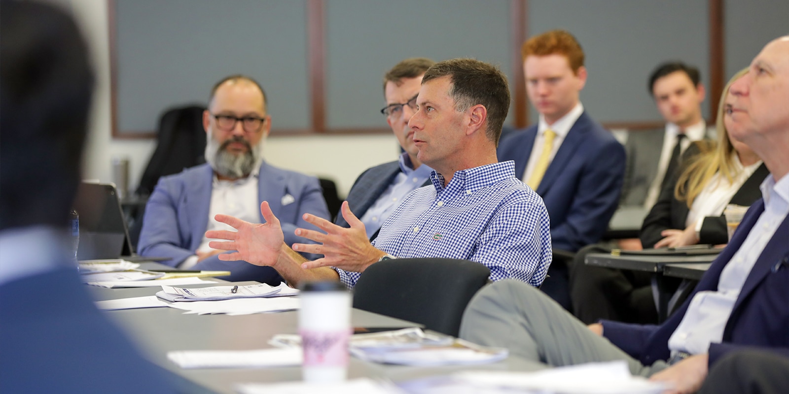 A Gator Student Investment Fund advisor actively engages in discussion during a panel session, surrounded by attentive students and professionals. The image highlights the collaborative, competitive environment students join when accepted into the fund.