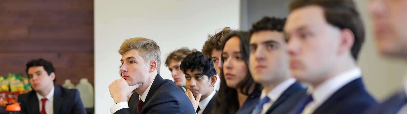 A focused group of professionally dressed University of Florida students listens intently during a Gator Student Investment Fund meeting, reflecting engagement and dedication to finance and investment education.