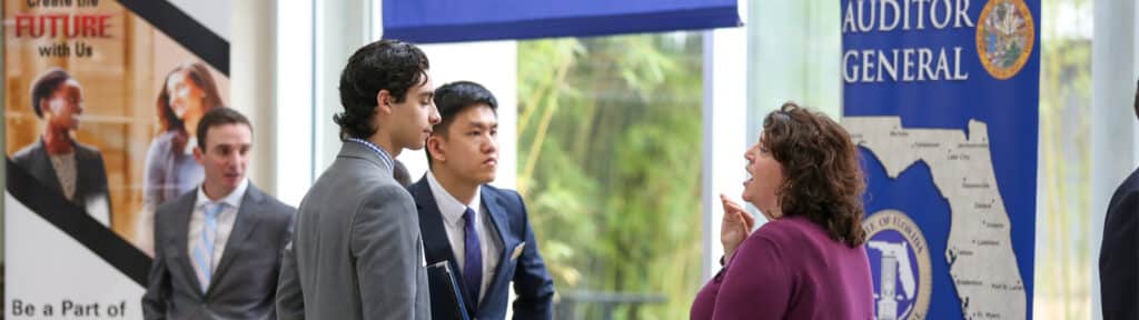A representative from the Florida Auditor General speaks with two students at a Warrington College of Business career fair booth.