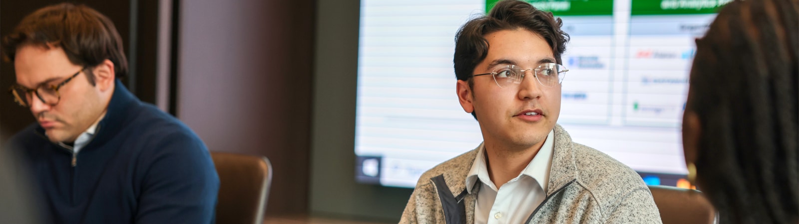 A student speaks during a research workshop discussion while others listen, with accounting data projected on a screen in the background.