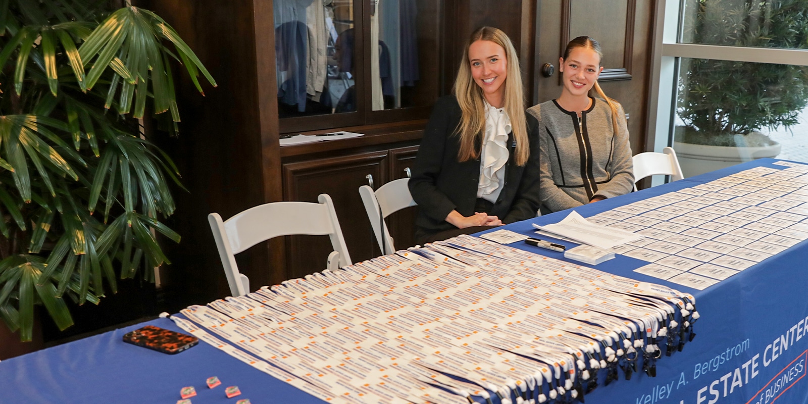 Two women at a check-in table prepare media passes for the Trends & Strategies Conference, with lanyards and badges neatly arranged.