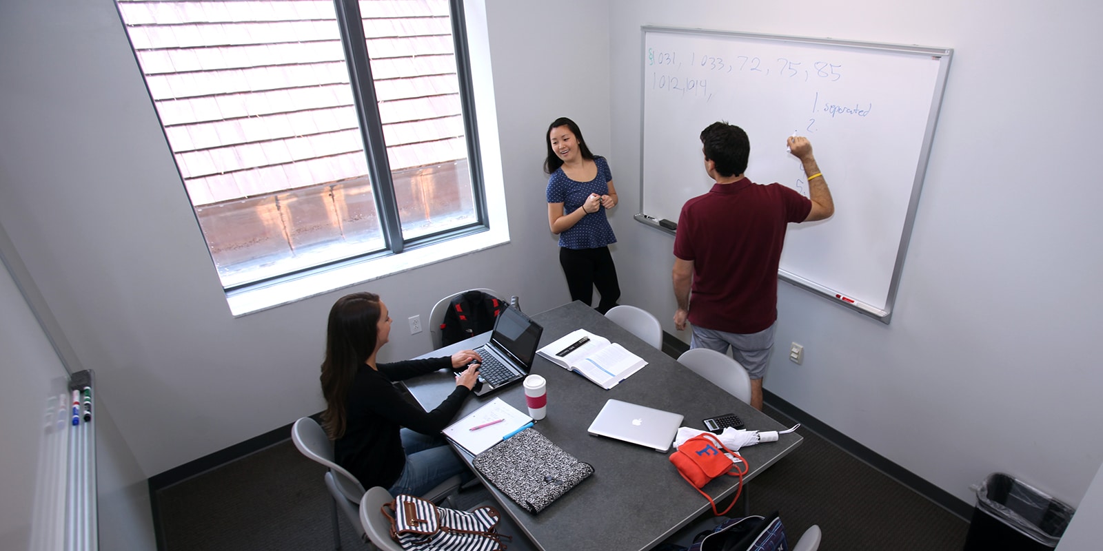 In UF Warrington's Fisher School of Accounting, three students collaborate on a project in a room with a table and a whiteboard