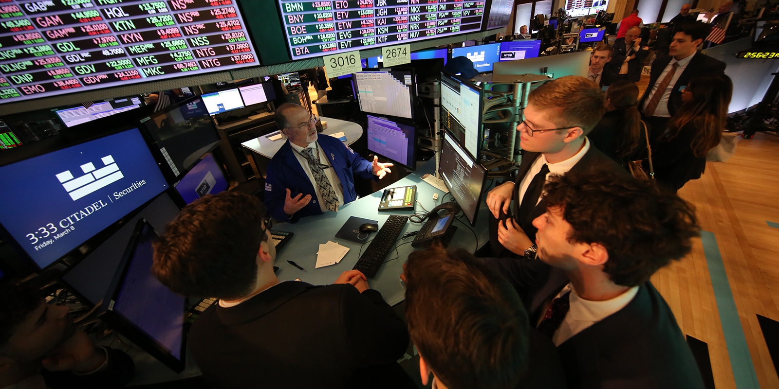 An instructor surrounded by computer monitors interacts with a group of MS in Finance students in the University of Florida's FinTech Research Center