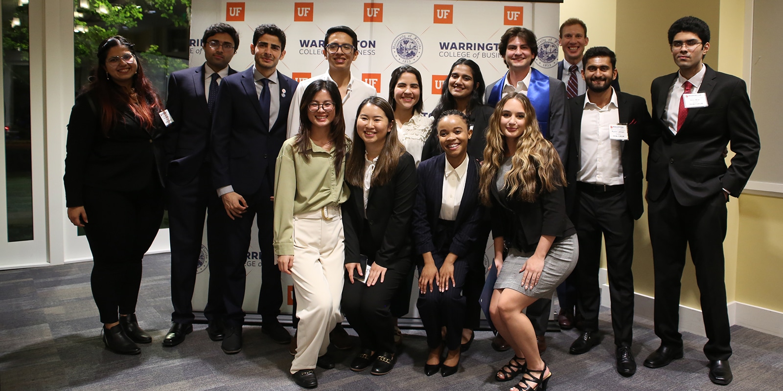 A group of students from UF Warrington's MS in ISOM - Data Science program pose in front of a wall with the college's logo