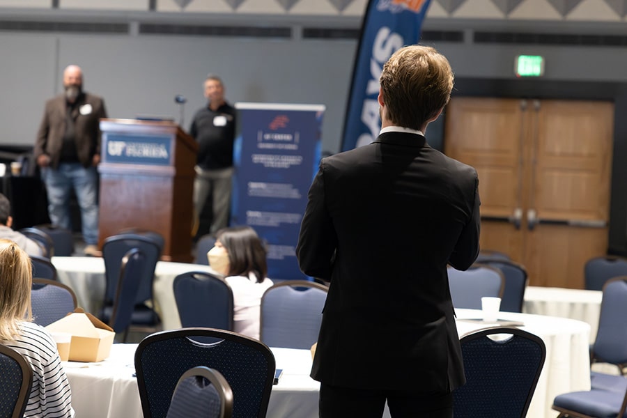 Student in professional attire standing up in front of presenting company recruiters to ask a question.