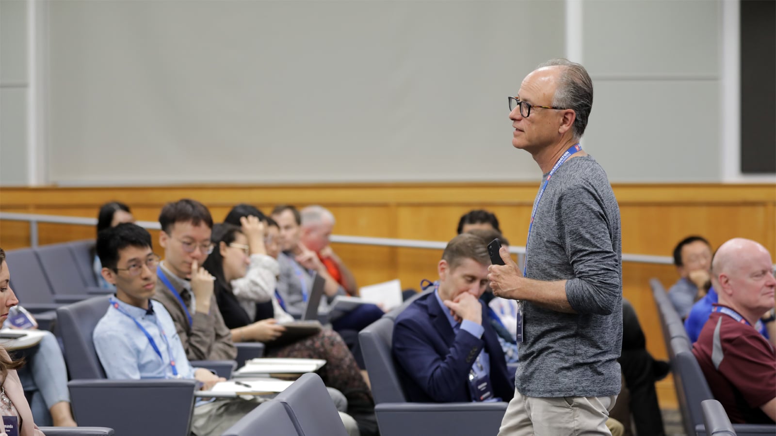 A speaker stands at the front of a lecture hall, addressing an audience of engaged professionals during a business analytics and artificial intelligence event.