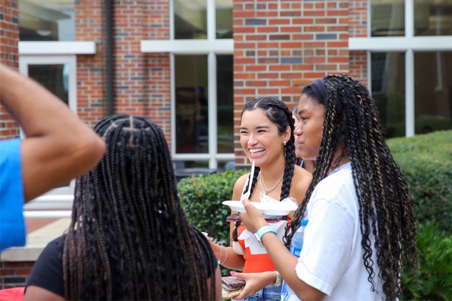 A group of students gathered outside on campus, smiling and chatting casually on a sunny day.