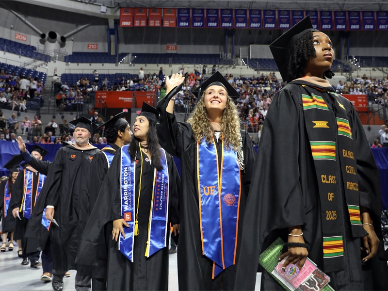 Graduates from professional MBA programs in caps and gowns wave to the audience during the Warrington College of Business recognition ceremony.