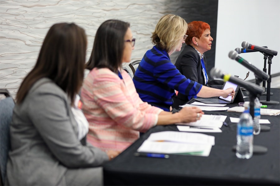 Four women, members of a professional panel, sit at a conference table with microphones and documents, focused on a discussion during a PURC executive committee meeting.