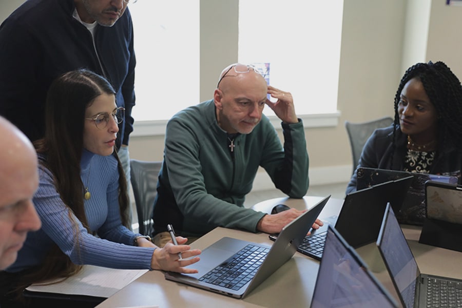 Group of older adults at a table of computers comparing and discussing research.