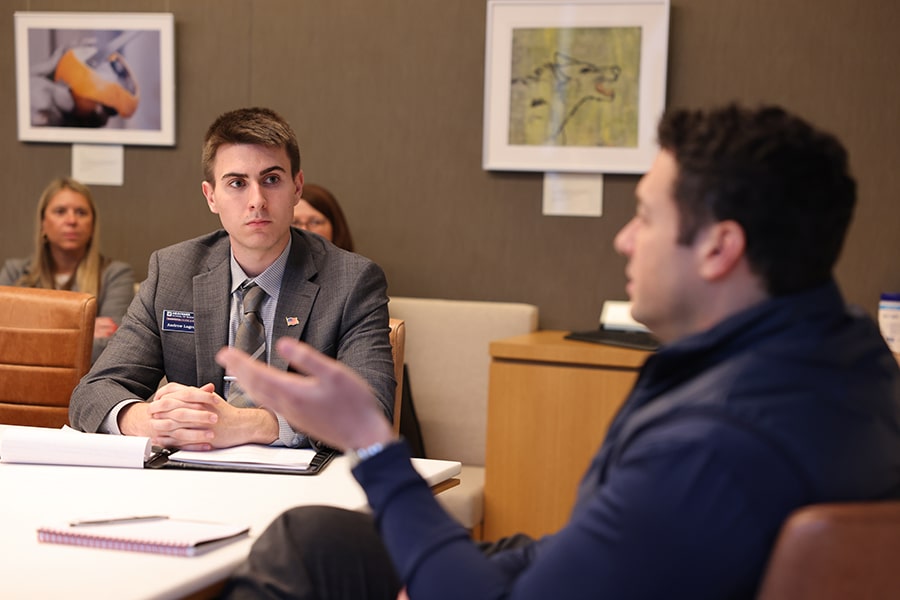 A student seated at a table speaking to an interviewer. 
