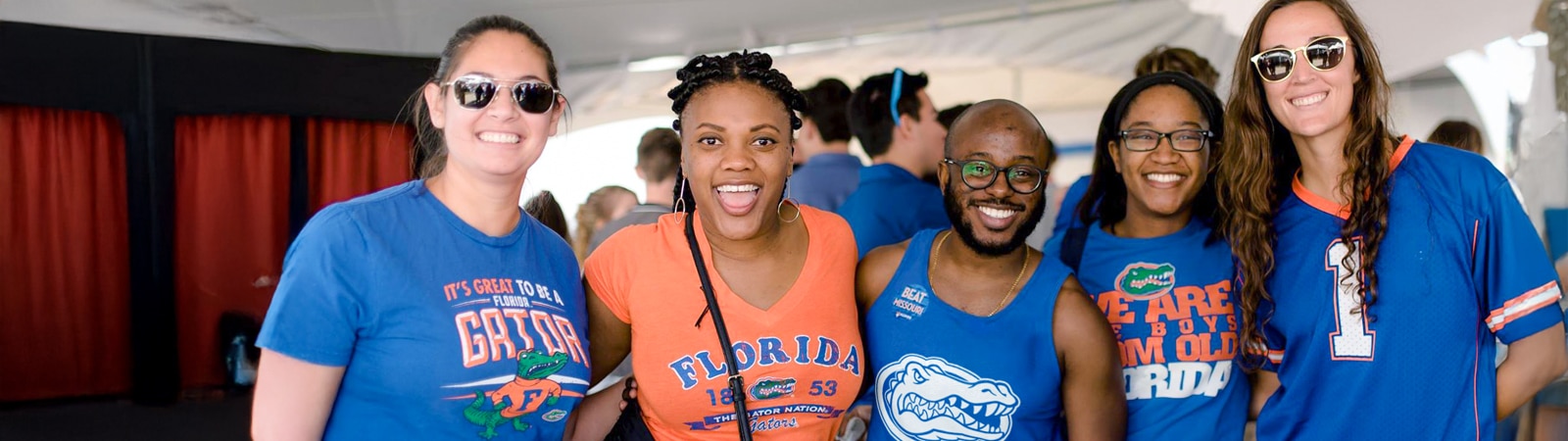 A diverse group of smiling people wearing University of Florida Gators apparel pose together in a lively social setting.