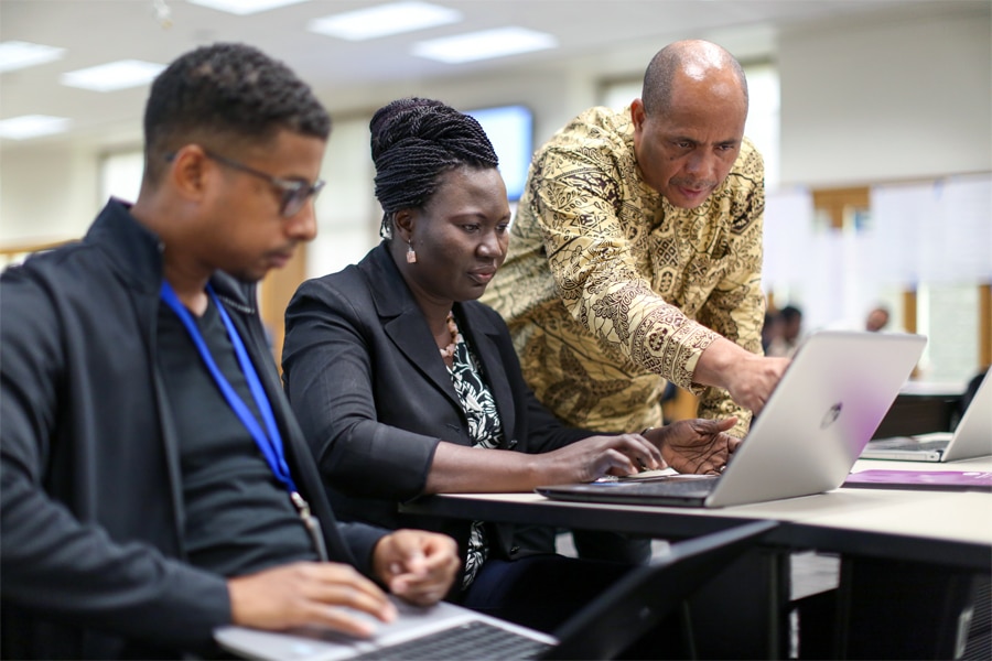 An instructor assists two participants with their laptops during a hands-on utility policy training session.