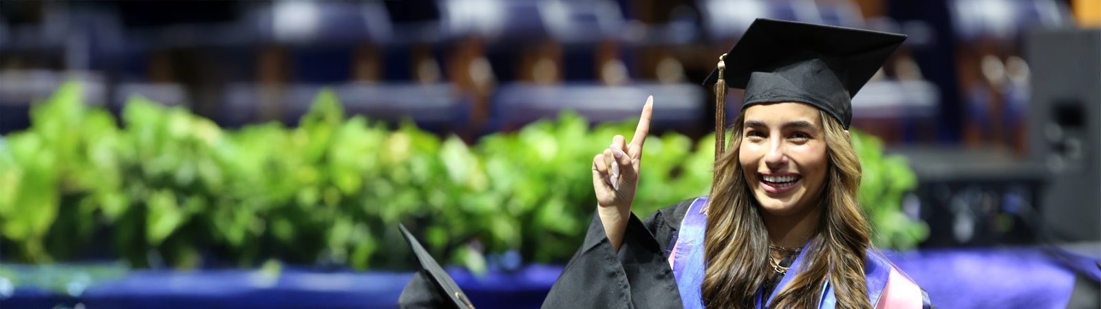 A smiling female student at commencement holding up the number 1 with her finger. 