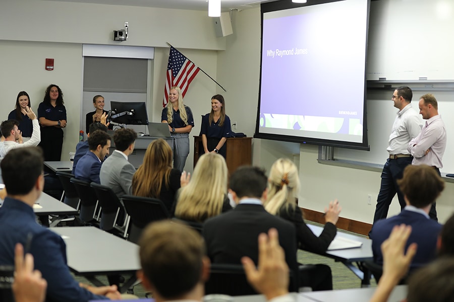 Executives speaking to a classroom of professionally dressed students. 