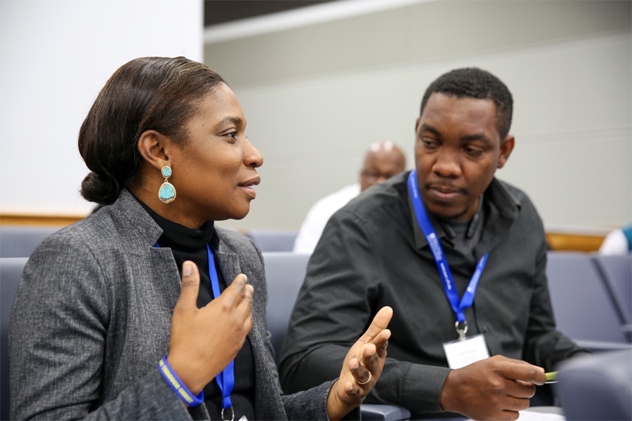 A woman and a man wearing blue lanyards engage in an in-depth conversation during a PURC training session, seated in a classroom environment.