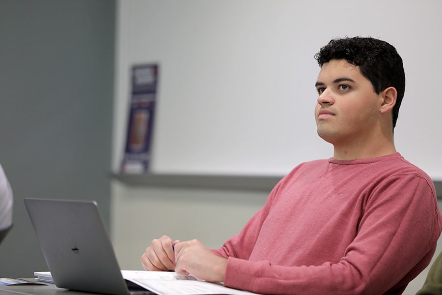 A young man sitting at his laptop with pen and paper.