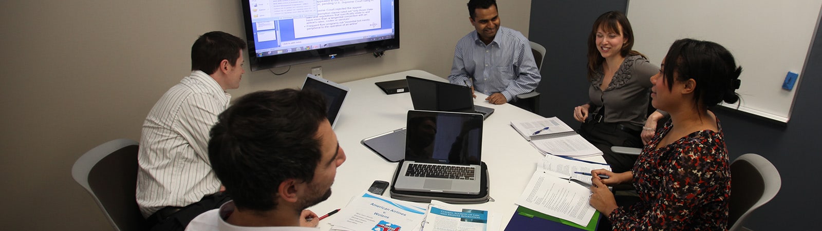 Group of older students at a table with their laptops and notes.