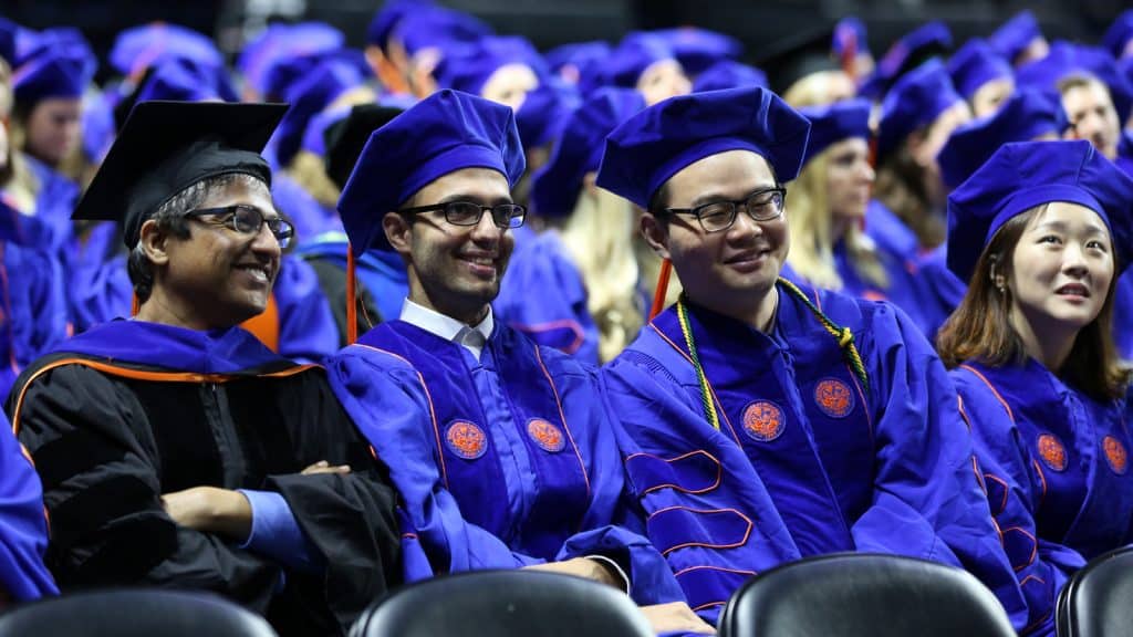 Ph.D. graduates in blue regalia celebrate at commencement alongside faculty.