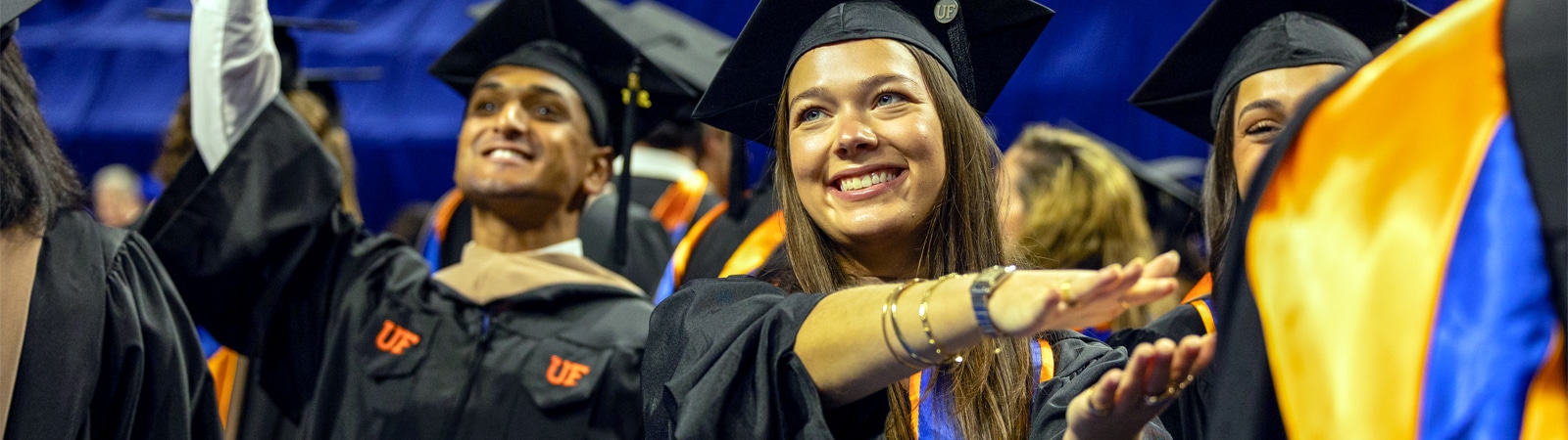 Graduates in black caps and gowns celebrate joyfully during a commencement ceremony, their faces bright with smiles and excitement.