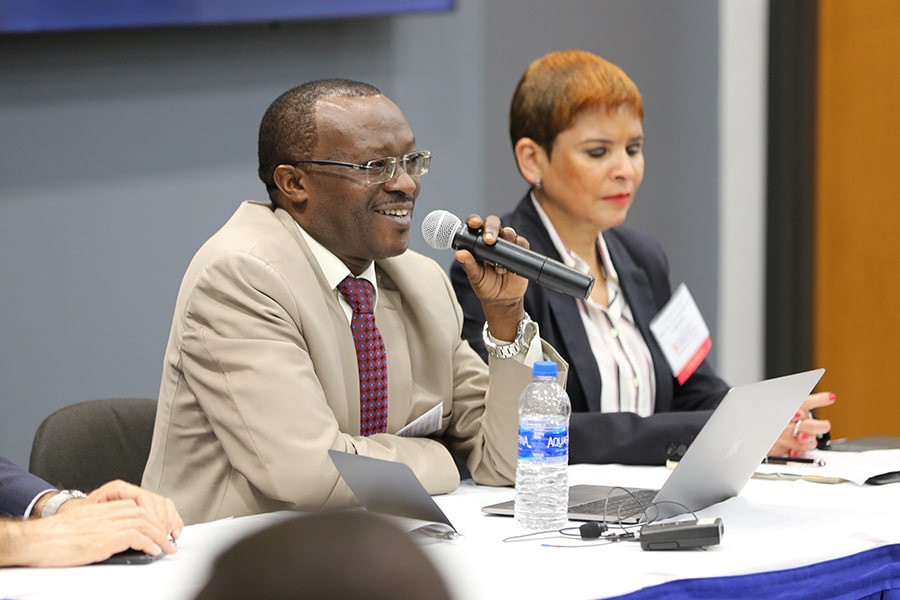 A man holding a microphone as he sits with a woman at an event's speaker table.