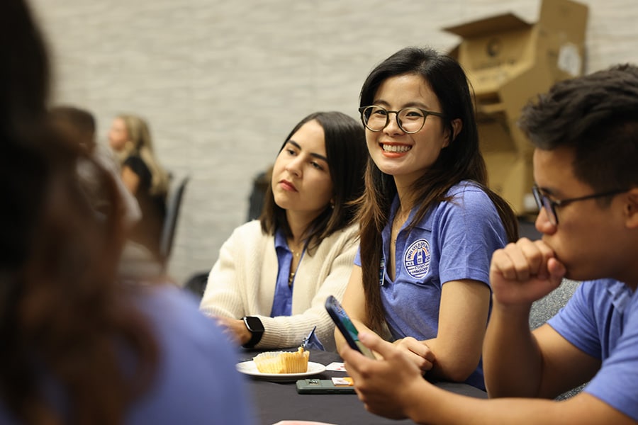 Student ambassador smiling at the camera as she sits with fellow ambassadors at a table.