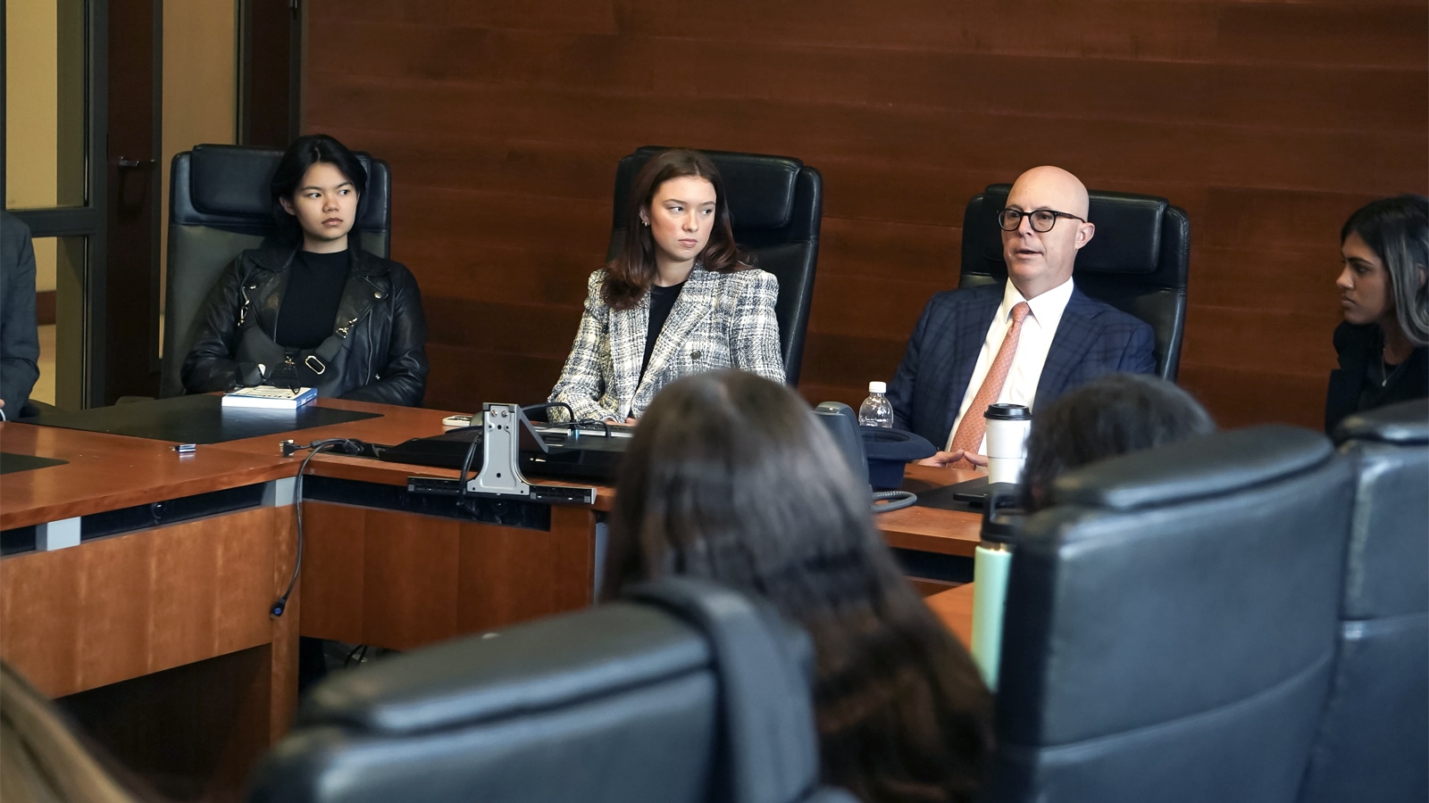 A diverse group of students and a faculty member engage in a discussion around a large conference table in a professional setting, focusing on investment portfolio management.