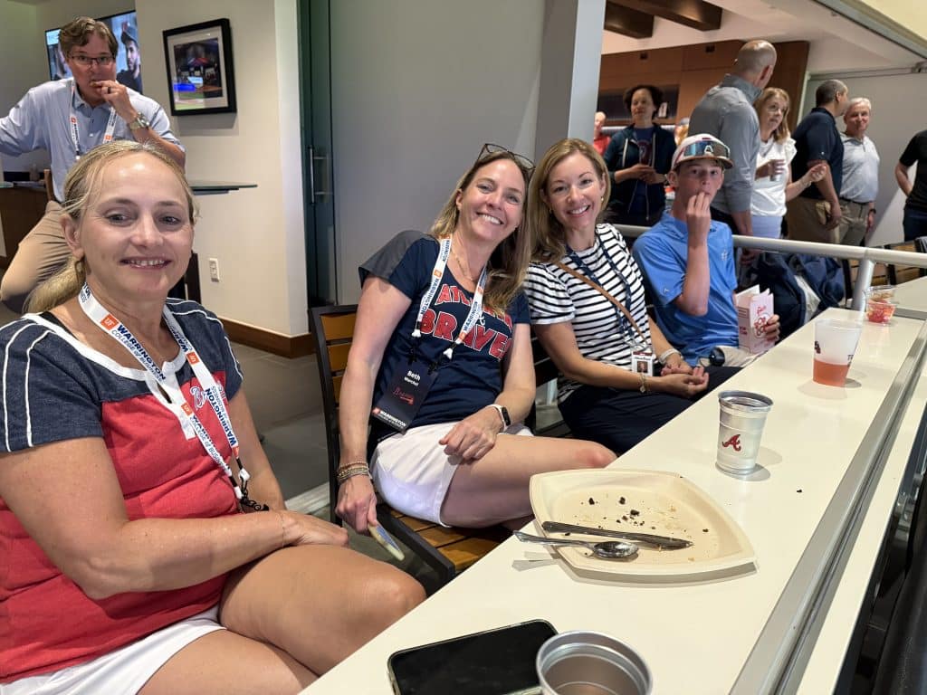 A group of women and a young man watch a baseball game during an alumni event. 