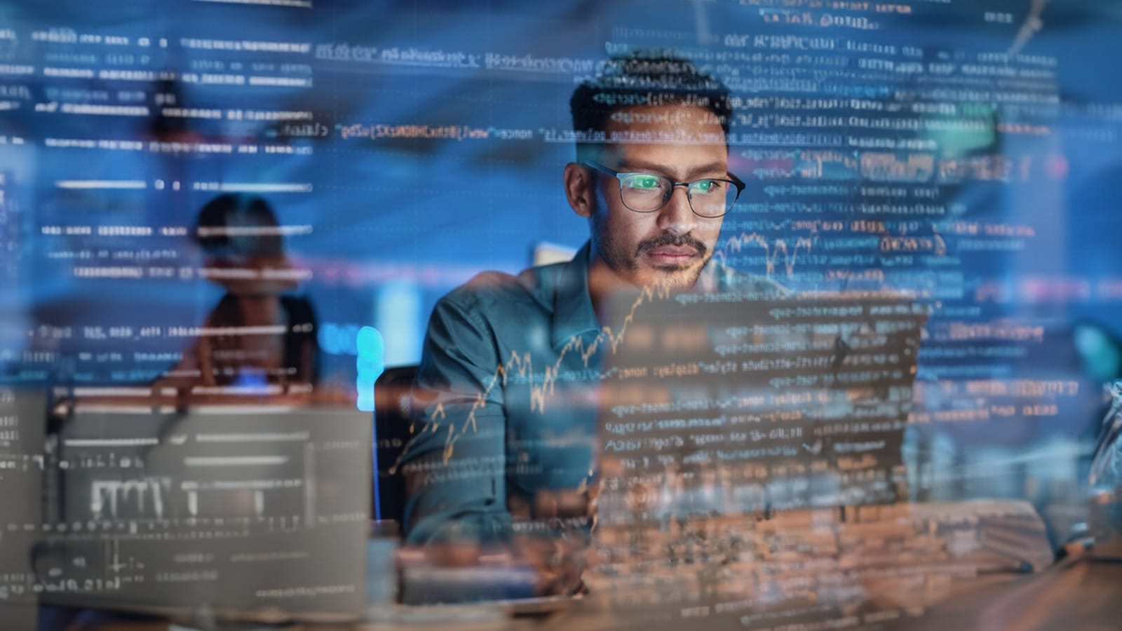 A man using a laptop with data visuals on screen. 