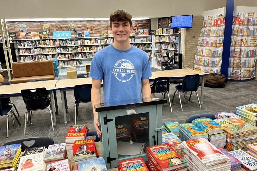 Chase Hartman stands in front of a table full of books and a little library box.