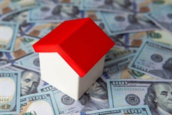 A tiny toy house with a red roof on $100 bills