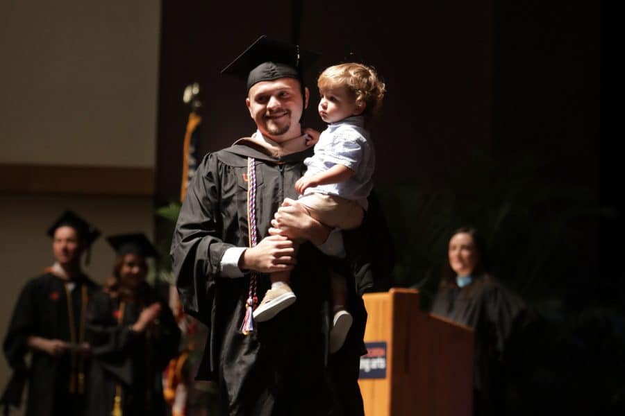 Kyle Hecker crosses the stage at graduation carrying his son in his arms.