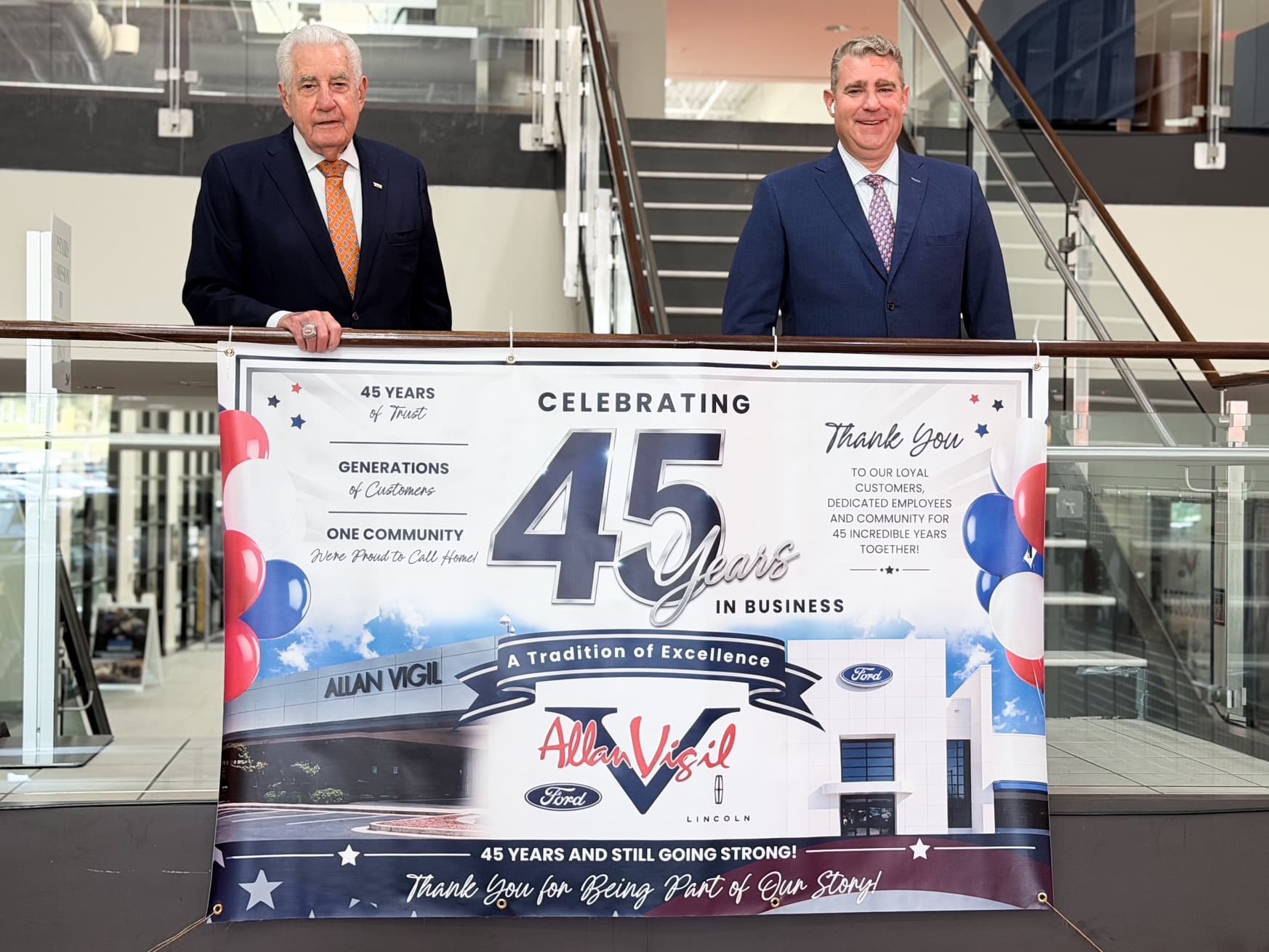 Allan Vigil and his son Michael Allan Vigil hold a sign celebrating 45 years in service of their car dealership. 